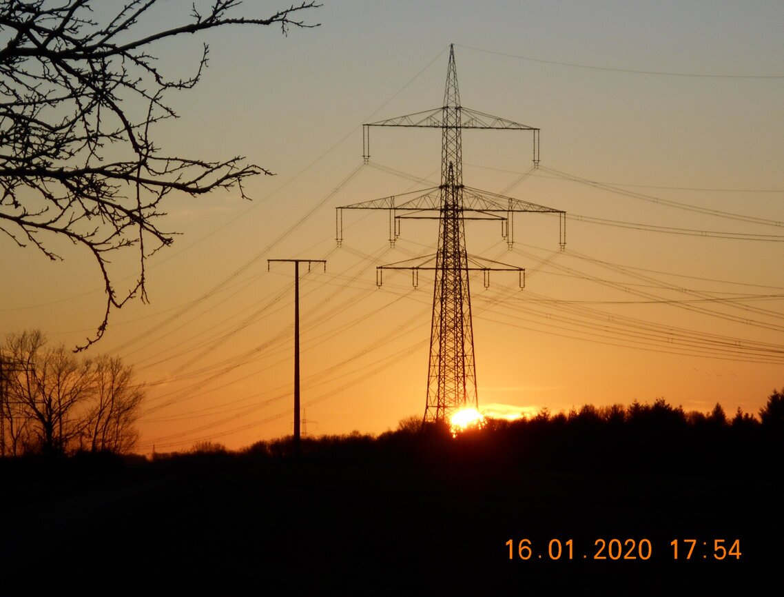 Sonne geht unter rechts von zwei Strommasten, Januar